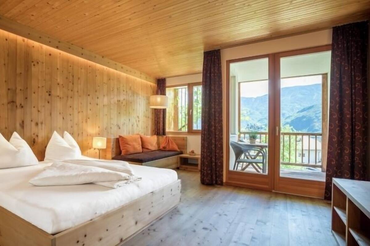 A wooden-paneled bedroom with a large bed, a sofa, and a balcony with a mountain view.