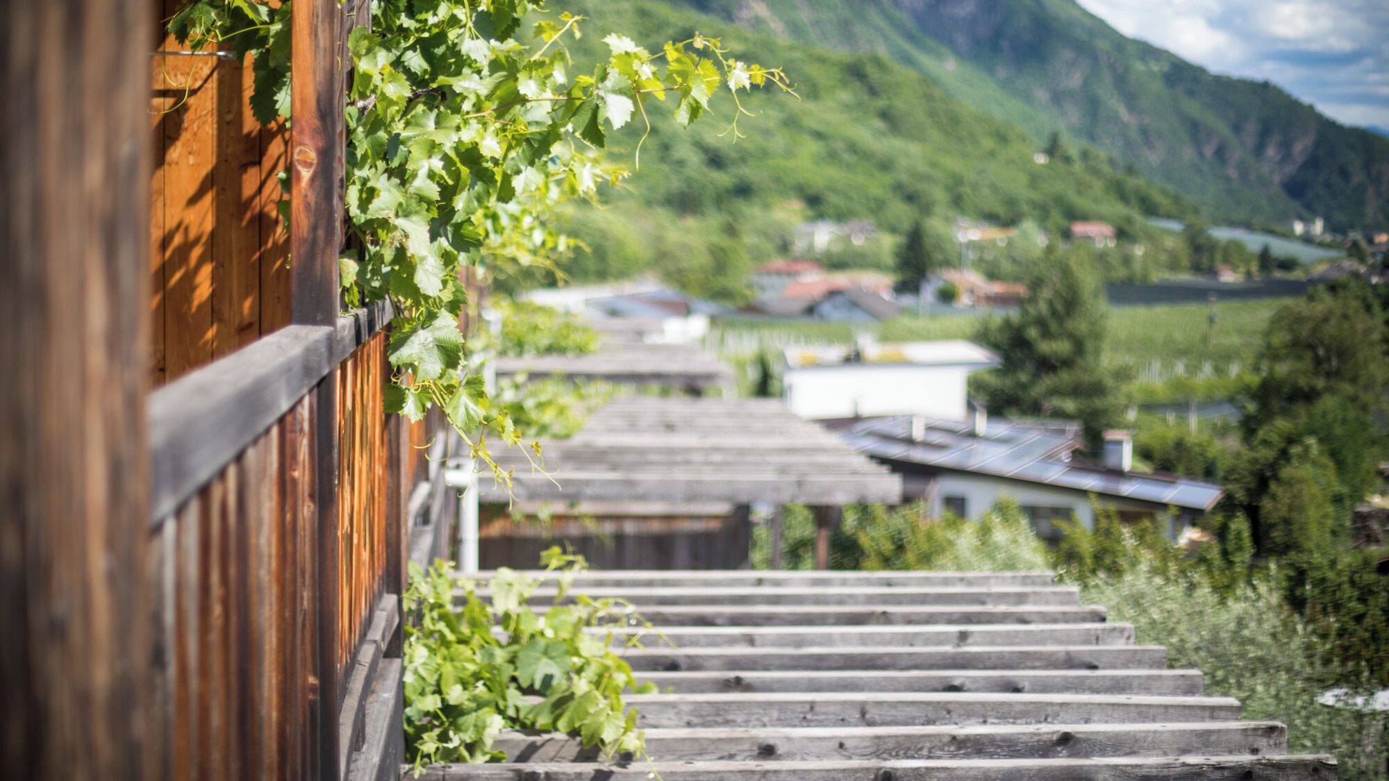 A wooden staircase leading to a mountain village with houses and greenery in the background.