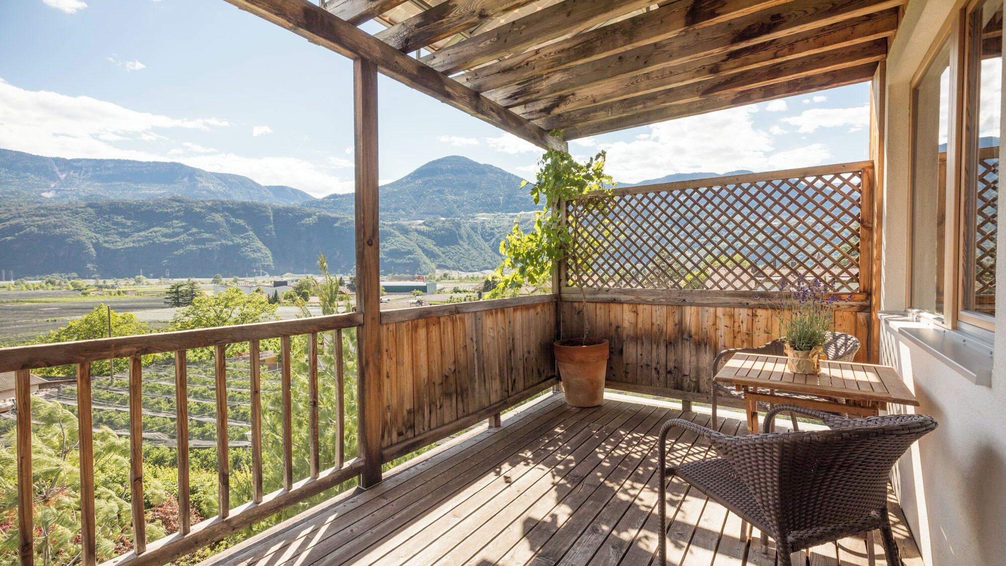 Una terraza de madera con una mesa y sillas, con vistas a un valle y montañas.