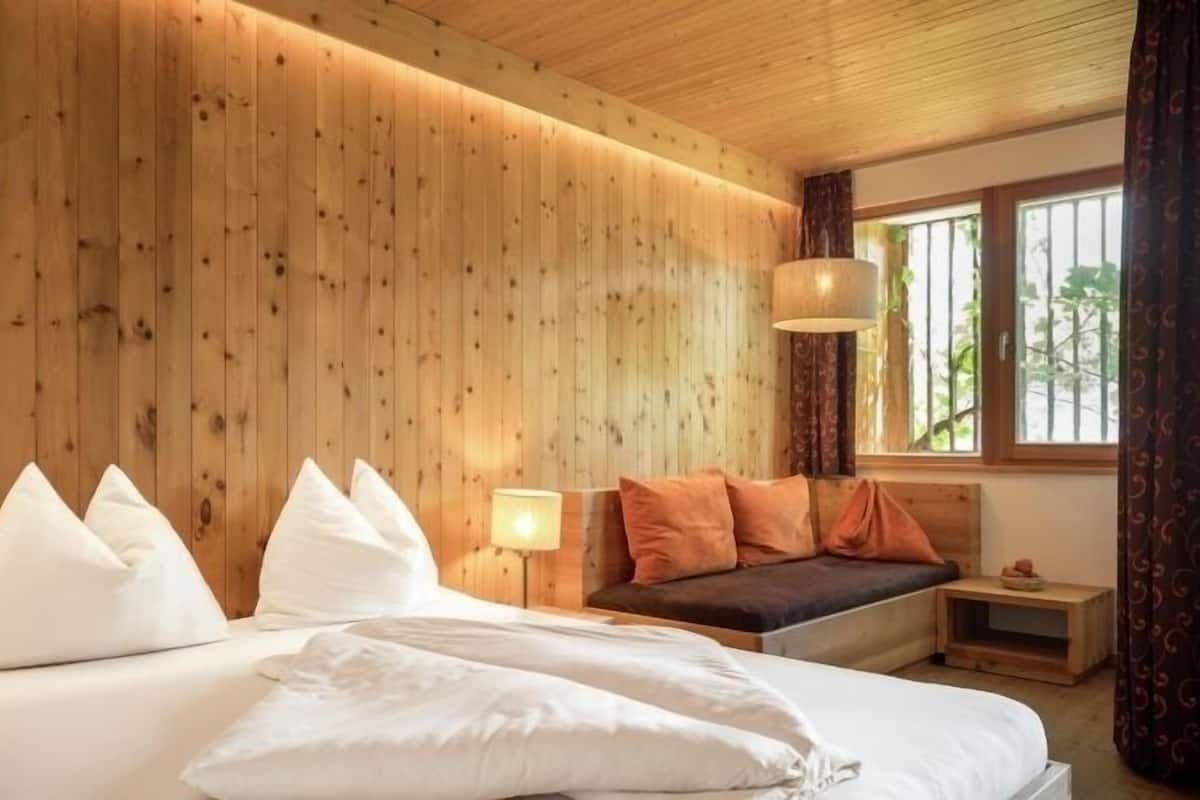 A wooden-paneled room with a bed, a bench, and a window.