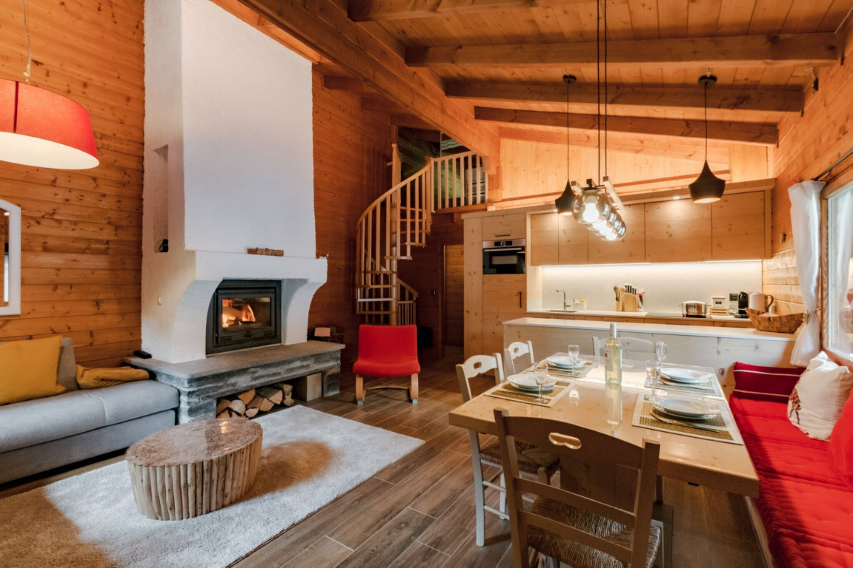 Un acogedor interior de cabaña con chimenea, paredes de madera, una zona de comedor y una escalera.