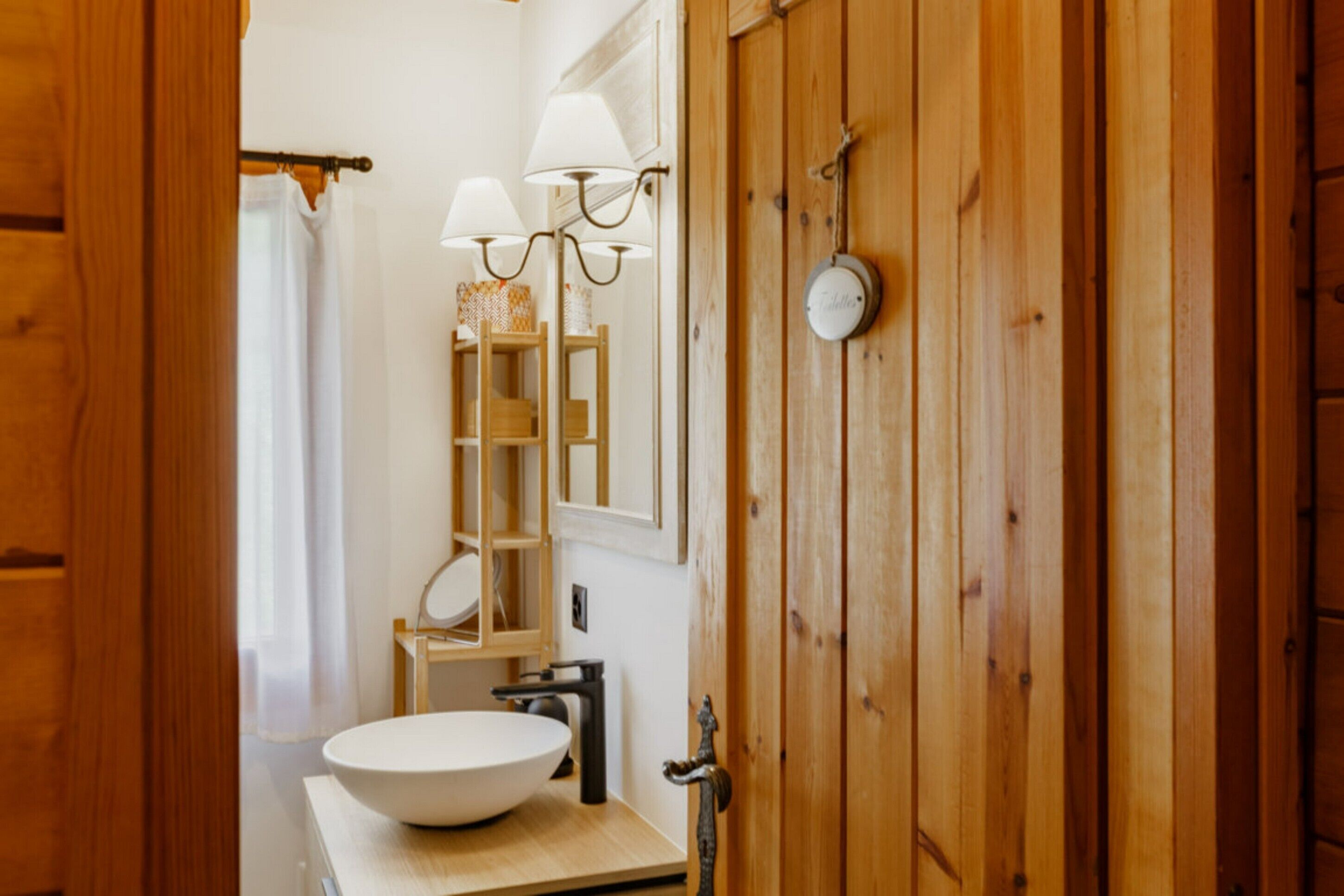 Ein Badezimmer aus Holz mit einem großen, weißen Waschbecken, einem Handtuchhalter und einem Spiegel mit Wandlampen.