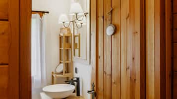 A wooden bathroom with a large white basin, a towel rack, and a mirror with wall-mounted lamps.
