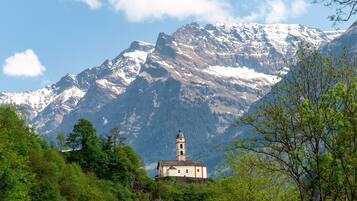 A mountain church with a bell tower, surrounded by snow-capped peaks and lush greenery.