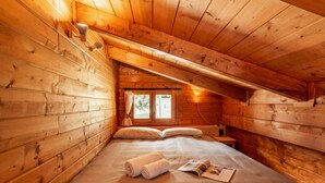 Ein Holzhütten-Zimmer mit einem Bett, Kissen, einem Fenster und Lektüre.