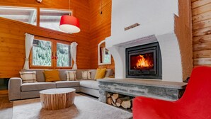 Ein Holzblockhaus-Interieur mit Kamin, einer Couch, einem roten Sessel und einem runden Holztisch.