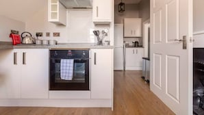 A modern kitchen with white cabinetry, an oven, and a countertop with various kitchen items. - Castle Garden View - Two Steps Away from Central Rochester High Street (Rochester)