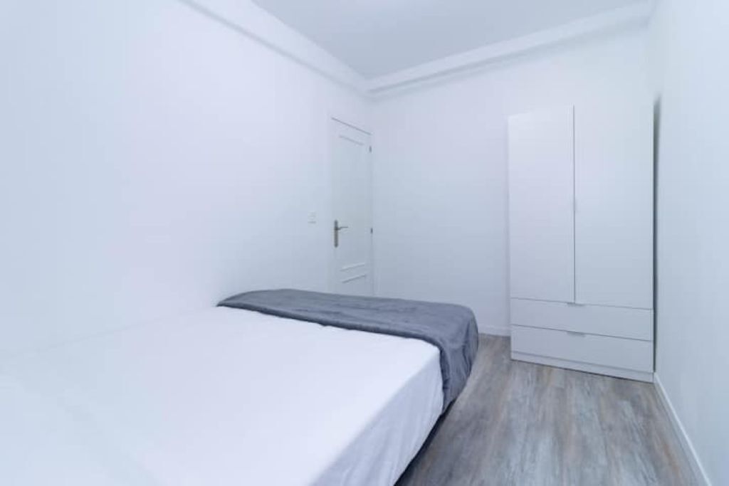 Una habitación pequeña y blanca con una cama, un armario y una puerta.