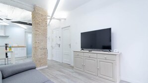 Een moderne woonkamer met een grijze bank, een televisie op een kast, en een stenen pilaar.