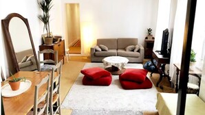 Una sala de estar con sofá, dos otomanas rojas, una mesa de centro, televisión y un comedor con mesa y sillas.