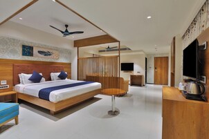 Habitación de hotel moderna con una cama grande, un escritorio con hervidor, televisión y ventilador de techo.