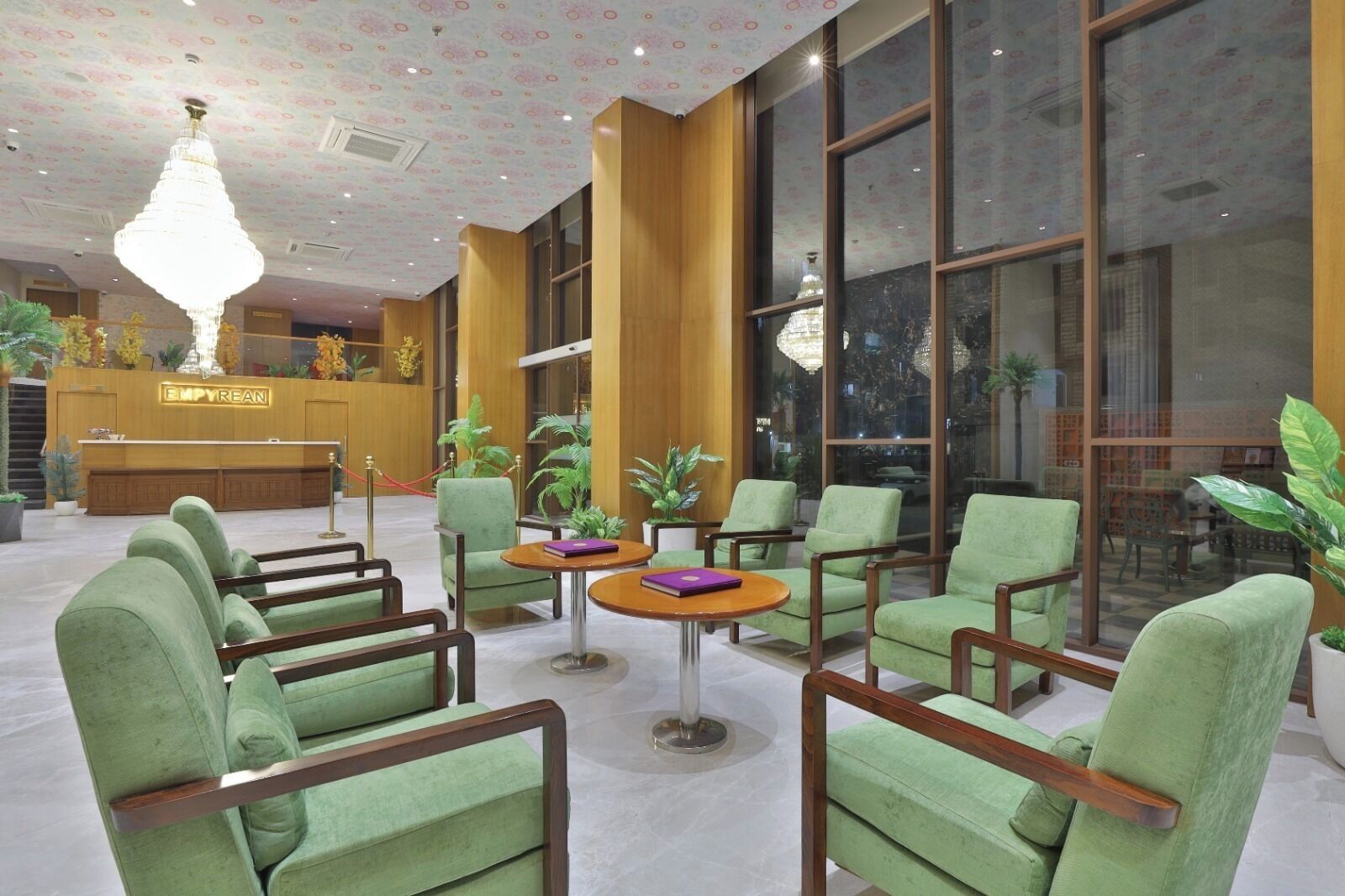 A lobby with green upholstered chairs, a reception desk, and large windows.