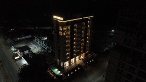 Un hotel de varios pisos con un llamativo letrero 'EMPYREAN', un área de piscina e ingreso bien iluminado.
