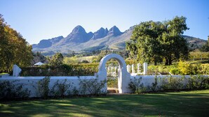 A white archway leading to a vineyard with mountains in the background. - Navarre Residence (Stellenbosch)