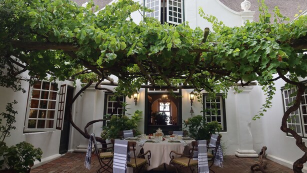 A white building with a covered outdoor dining area, featuring a table set for four, surrounded by chairs and potted plants. - Navarre Residence (Stellenbosch)