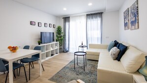 Ein modernes Wohnzimmer mit einer Couch, einem Esstisch mit Stühlen, einem Fernseher und einem kleinen Beistelltisch.