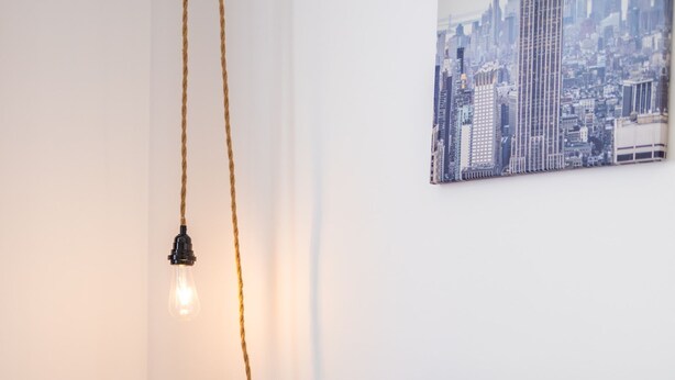 Ein ordentlich bezogenes Bett mit Kissen, ein Nachttisch mit Buch und Kerze sowie ein Tablett mit Croissants und Getränken.