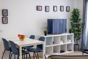 A modern living room with a white TV stand, a flat-screen TV, a dining table with chairs, a potted plant, and framed pictures on the wall. - Beach - In the Center of the Village (Alcobaça)