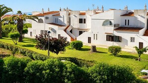 A white building with red-tiled roofs, a staircase, and a well-maintained garden with palm trees and shrubs. - Fully equipped, by the sea in a quiet residential area near Olhão. (Moncarapacho)