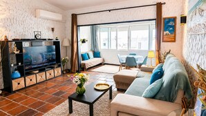 A living room with a TV, sofa, coffee table, and a view of the outside. - Fully equipped, by the sea in a quiet residential area near Olhão. (Moncarapacho)