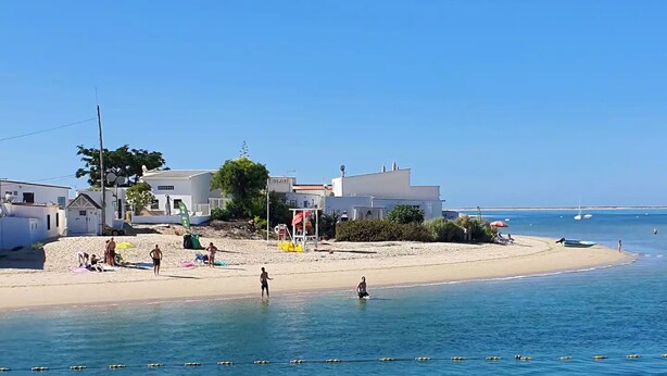 A beachside property with a sandy beach, clear blue water, and white buildings. - Fully equipped, by the sea in a quiet residential area near Olhão. (Moncarapacho)