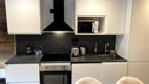 Cozinha compacta com armários brancos, coifa preta, micro-ondas, fogão, pia e lava-louças.