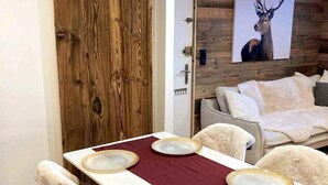 Uma área de jantar com porta de madeira, mesa branca com toalha vermelha e quadro de um veado na parede.