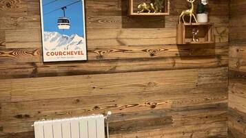 Una habitación con paneles de madera, un cartel de Courchevel, un radiador y una toalla doblada cuidadosamente sobre el suelo.