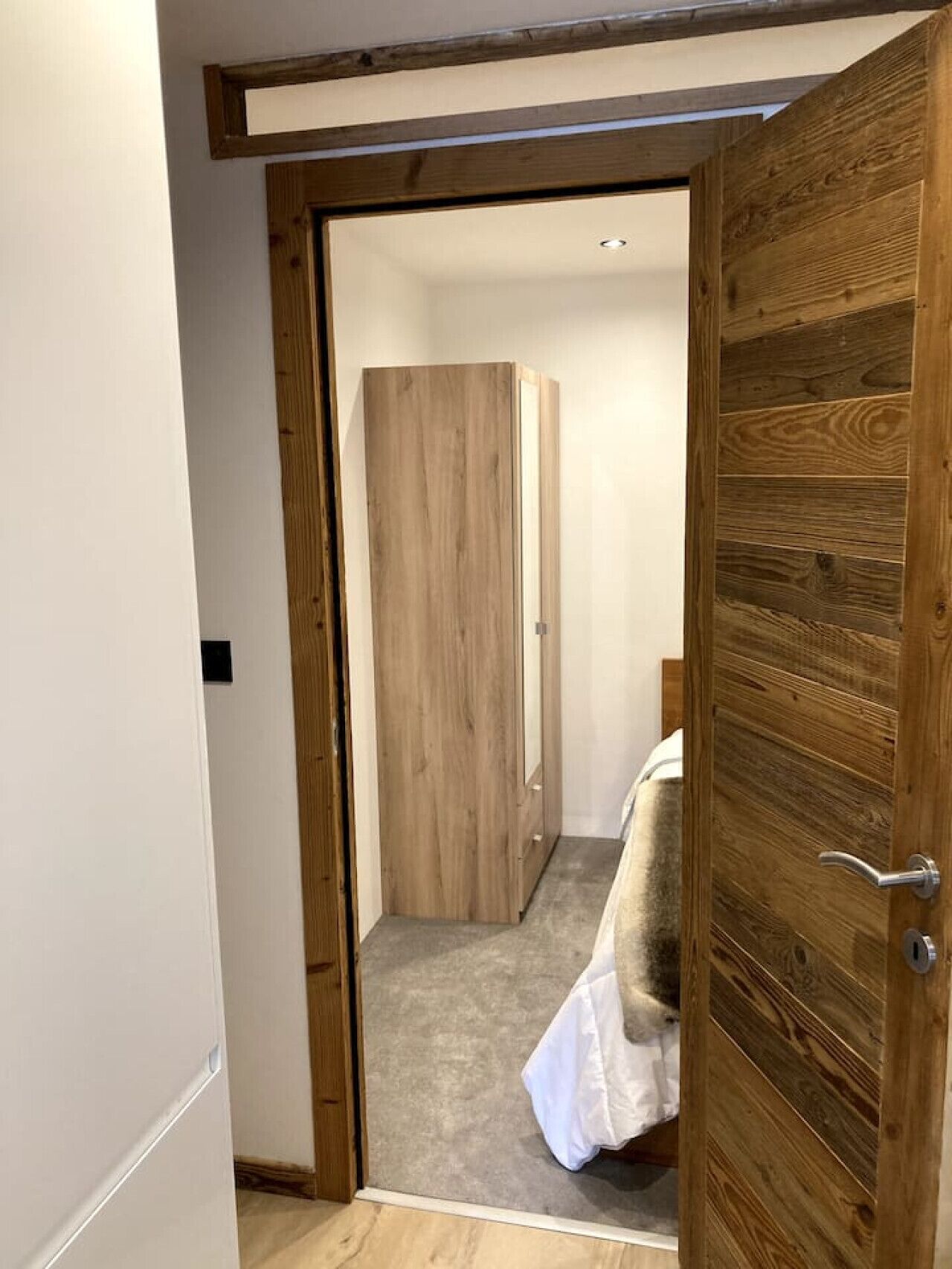 Une porte en bois qui donne sur une chambre à coucher, où se trouvent un lit et une armoire.