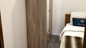 A bedroom with a wooden wardrobe, a bed with a white and blue bedspread, and a grey carpet.