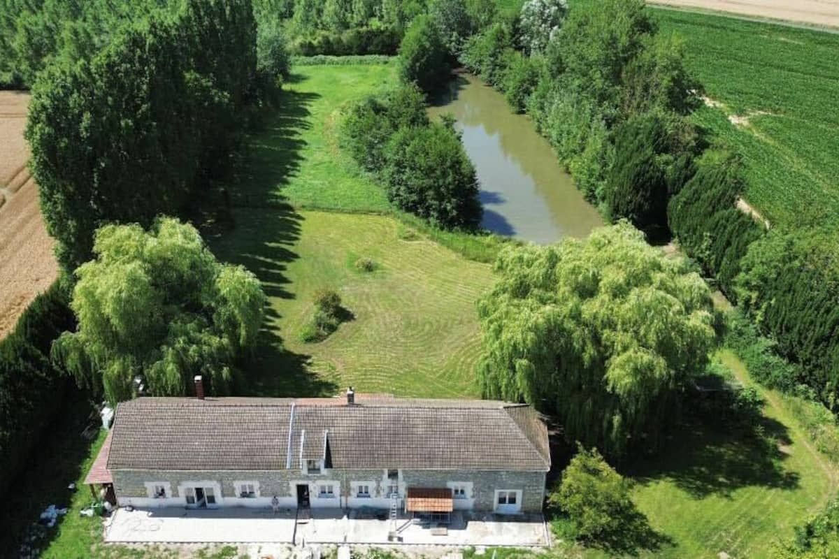 An aerial view of a house with a tiled roof, surrounded by fields and a river.