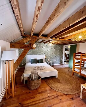 A bedroom with a wooden ceiling, a bed with pillows, a bedside lamp, a woven basket, and a wooden chair. - Le Moulin Saint-Nicolas (Maizy)