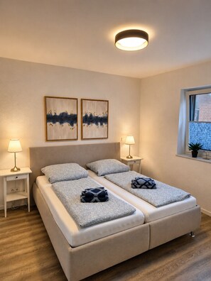 Ein Schlafzimmer mit einem Doppelbett, Nachttischen mit Lampen, zwei an der Wand hängenden Kunstwerken und einem Fenster mit Blick.