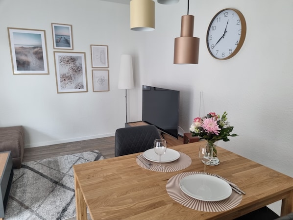 A modern dining area with a wooden table set for two, a flat-screen TV, and framed artwork on the wall. - "glückauf" - Gemütliche Ferienwohnung Nahe Steinhude (Hagenburg)
