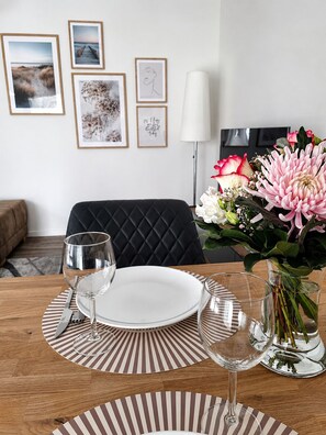A dining table set with plates, cutlery, and glasses, a vase with flowers, and framed pictures on the wall.