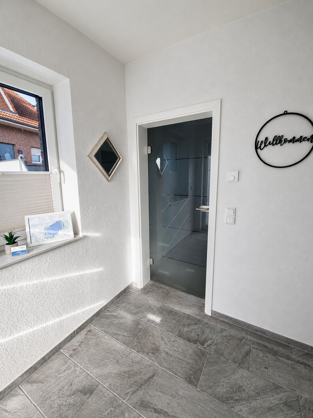 Un pasillo con una puerta que da a un baño, un estante pequeño con un mapa enmarcado y un cartel de bienvenida en la pared.