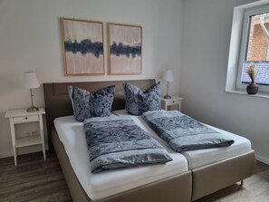 Ein Doppelbett mit Kopfteil, zwei Nachttische, ein Fenster mit Blick und zwei an der Wand befestigte Gemälde.