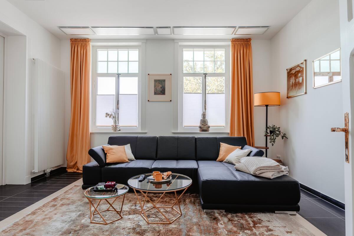 A modern living room with a black sectional sofa, a glass coffee table, and a patterned rug.