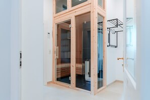 Moderni huone, jossa on puinen vaatekaappi, lasiovi ja seinälle kiinnitetty pyyhekoukku.