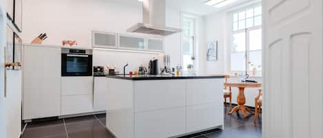 Une cuisine moderne avec des meubles blancs, un four encastré et un grand îlot central doté d’un plan de travail noir.