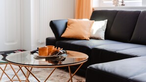 Een moderne woonkamer met een glazen salontafel, een donkere bank met kussens, en een radiator op de achtergrond.