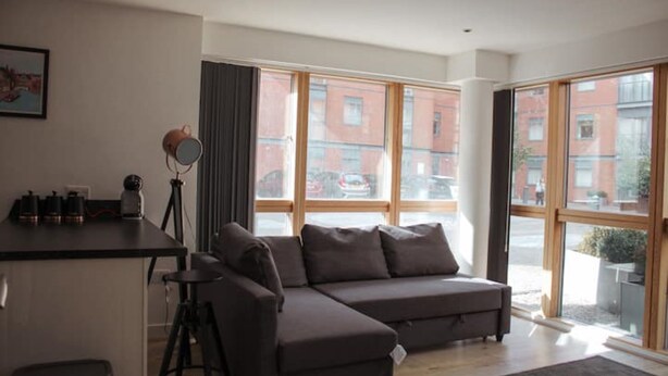 En moderne stue med sofa, lille bar og store vinduer med byudsigt.