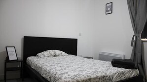 Et soveværelse med en seng, et natbord, et billede i ramme og en radiator.