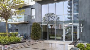 A modern building with a glass entrance, a parking area, and a small tree.