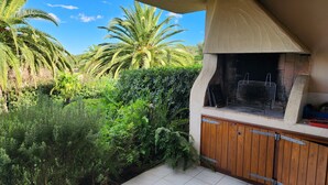 A patio with a built-in grill, surrounded by lush greenery and palm trees. - A 250 m de la Plage de Favone, Appartement vue mer Avec Terrasse de 30m2 (Conca)