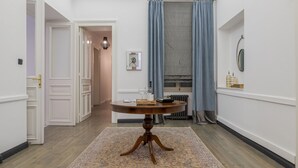Un couloir avec une table ronde en bois, un tapis à motifs, un radiateur et des rideaux bleus.