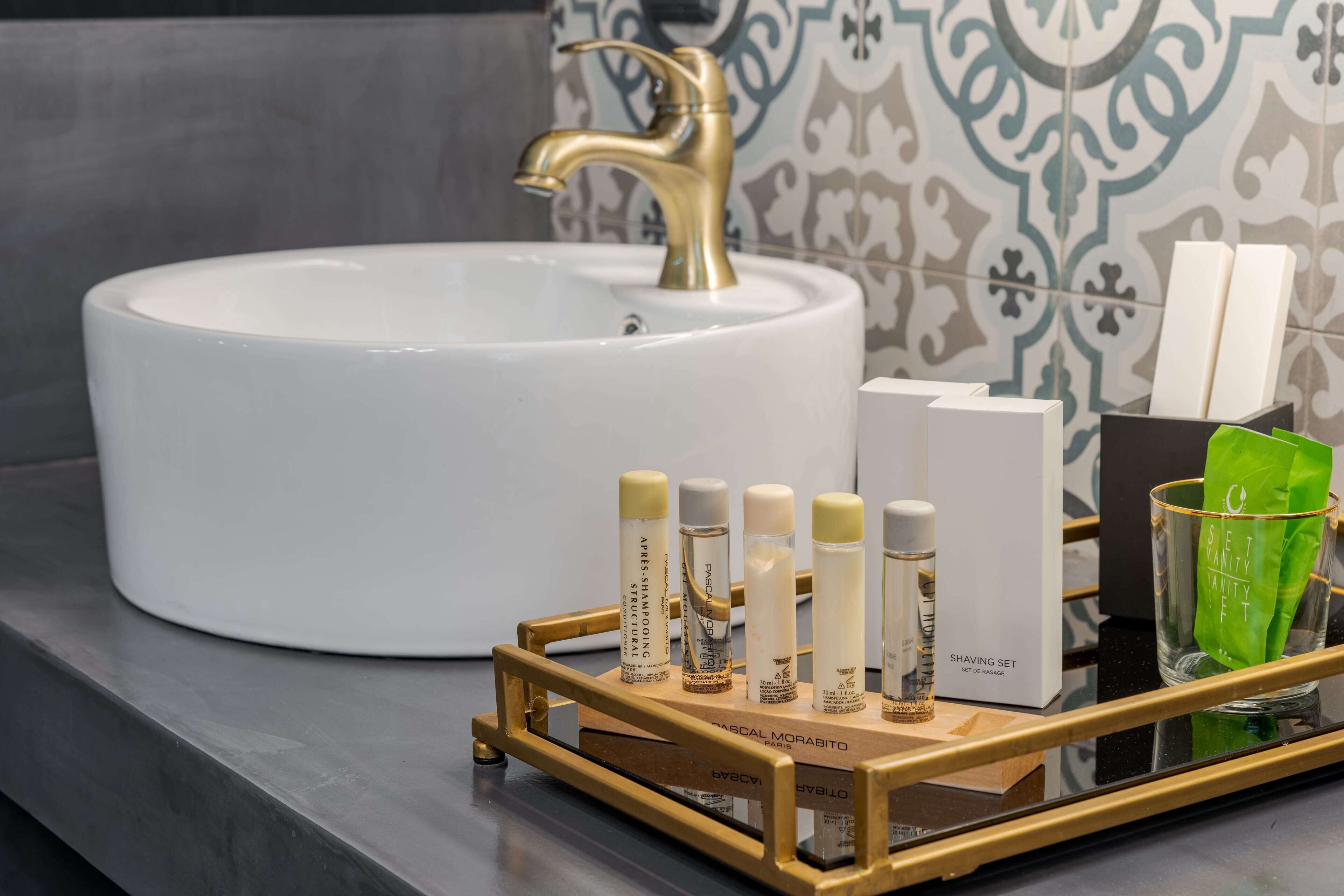 A bathroom with a white sink, gold faucet, and a tray with grooming products.