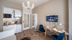 A modern kitchen with a microwave, oven, and white cabinets. There's a dining area with a wooden table, two chairs, and a TV mounted on the wall displaying various apps. - Old Town - Studio Petrin Tower (Prague)