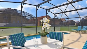 Et overdækket udendørs område med swimmingpool, liggestole og et bord med blomster.