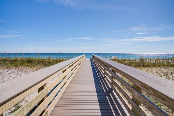 A wooden boardwalk leading to a beach with clear blue water.